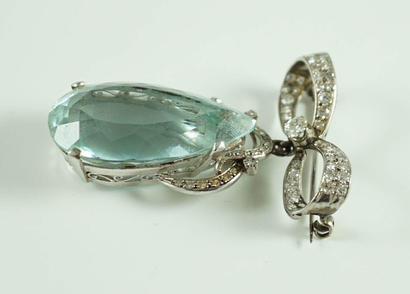 A mid 20th century continental white gold, facet cut pear shaped aquamarine and diamond set drop pendant, on a diamond set ribbon bow brooch